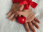 Zdjęcie pierwsze przedstawia rączki związane czerwoną kokardką i z serduszkiem pomiędzy dłońmi.
